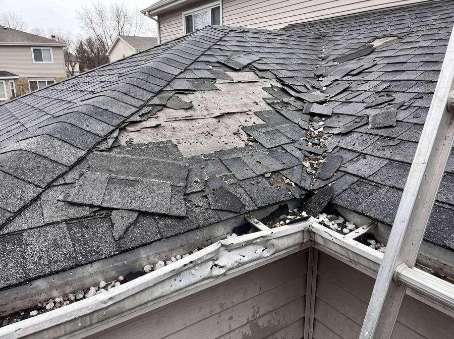 A suburban roof with shingles torn away by hail